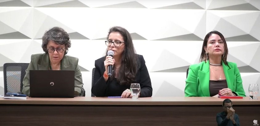 A imagem mostra três mulheres sentadas lado a lado atrás de uma mesa, participando da audiência....