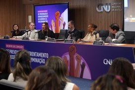 No registro, há uma bancada, com um banner longo do evento em cores roxo e rosa. Atrás do espaço...