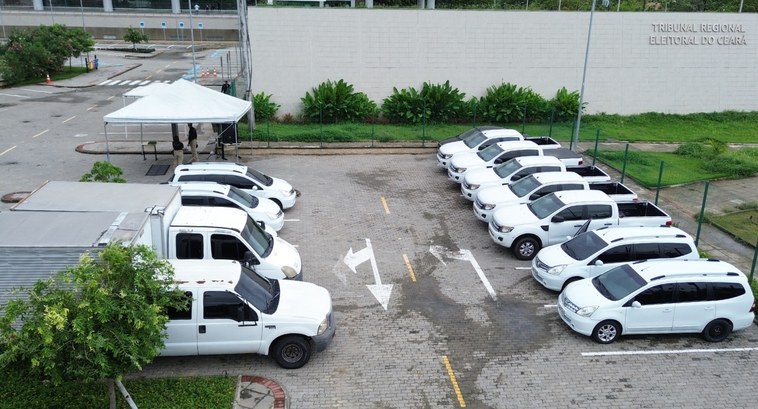 Registro fotográfico feito durante a cerimônia de doação dos veículos. Há um estacionamento aber...