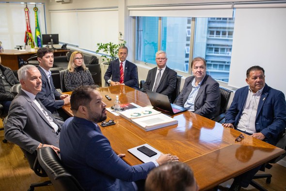 Registro fotográfico feito na reunião. Nele, dez pessoas estão sentadas em volta de uma mesa gra...